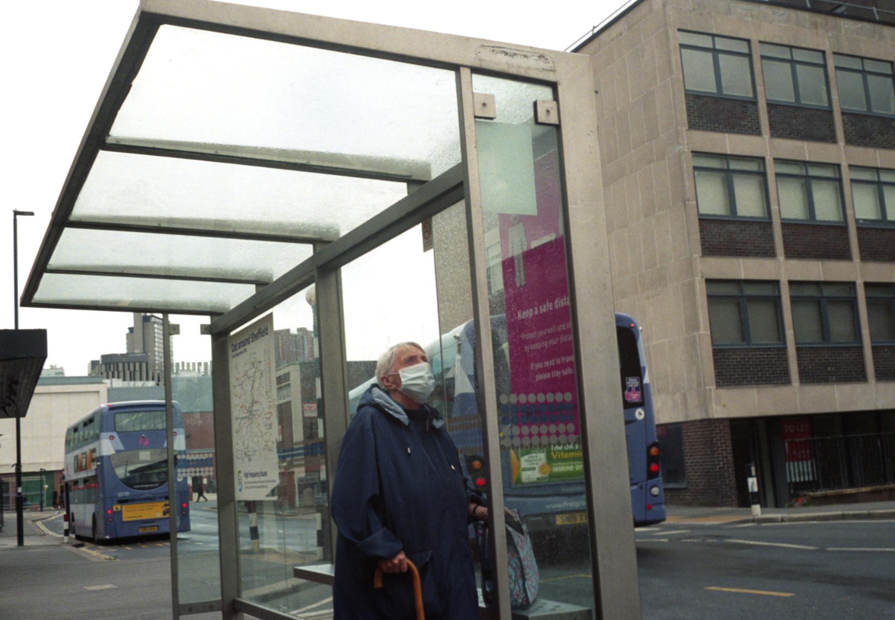 an elder lady at a bus shelter weaing a surgical mask