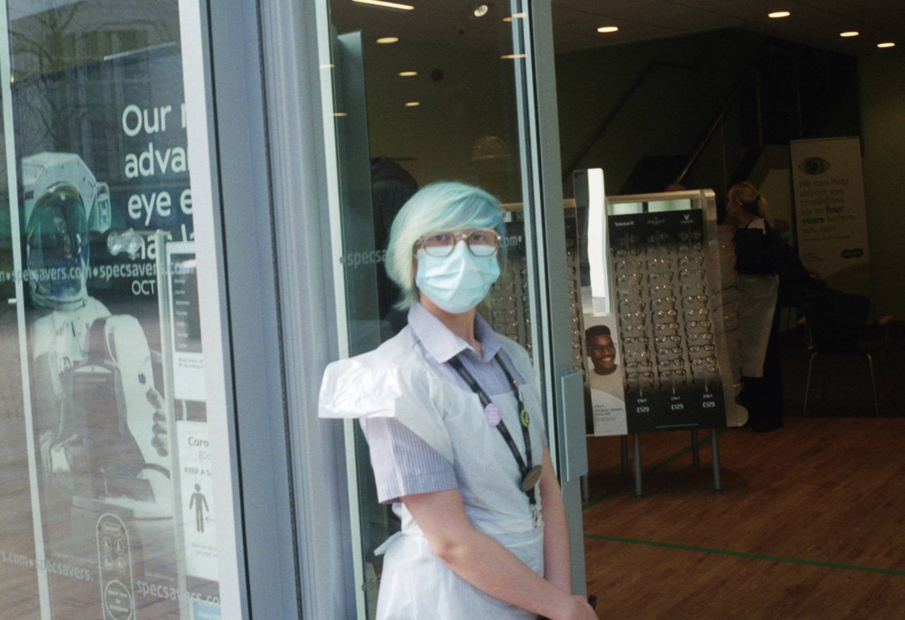 A retail worker wearing PPE with blue face mask and blue hair