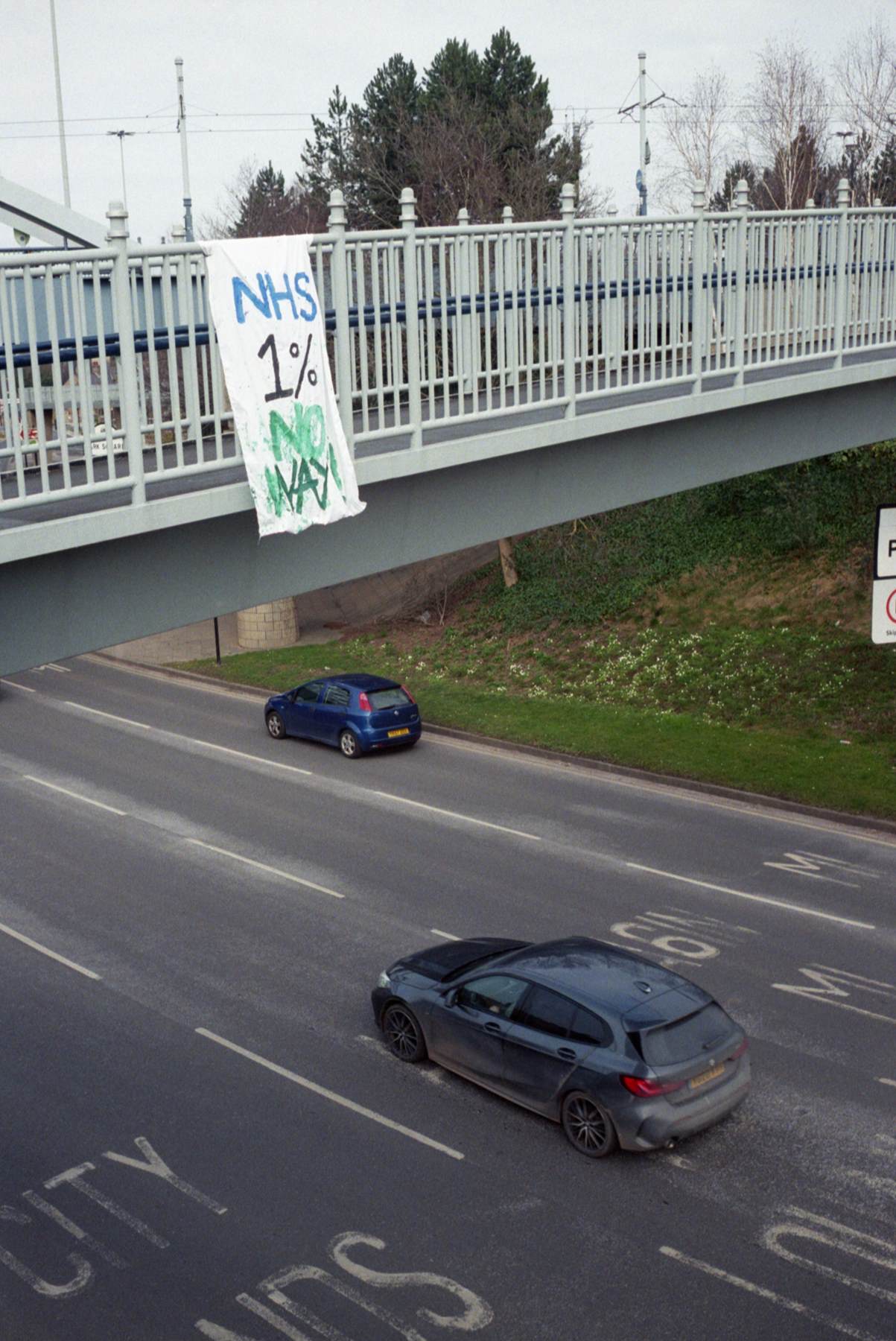 a protestor sign hangs from walkway over road protesting a weak NHS payrise 