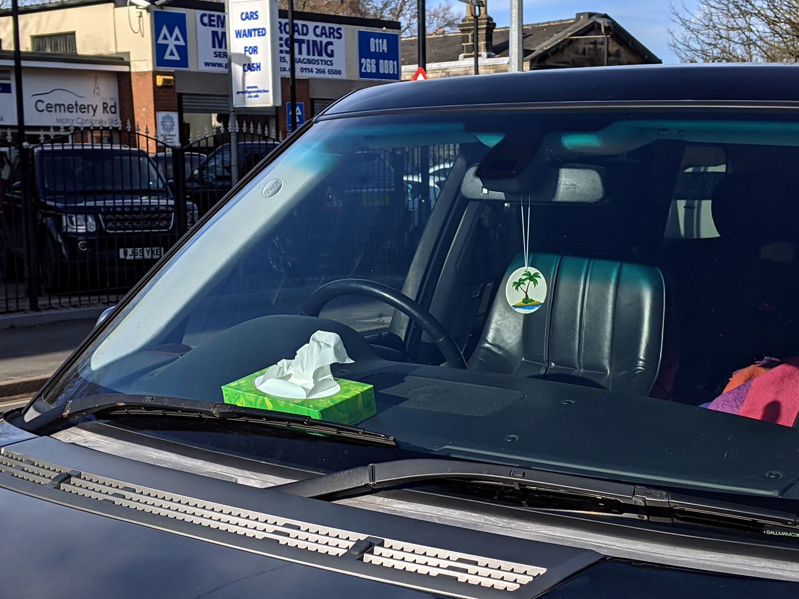 a box of tissues sits on a car dashbard with a dessert island hanging in the window